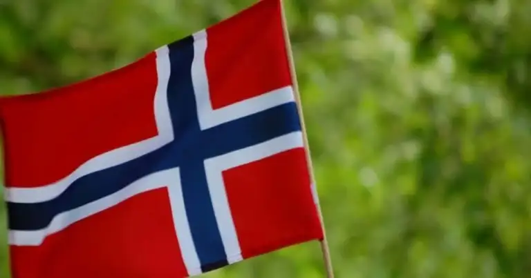 Bandera roja de Noruega con cruz azul ondeando en viento sobre fondo verde