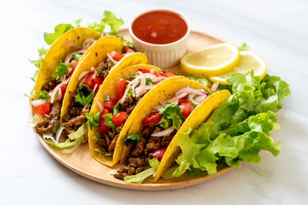Tacos rellenos de carne con lechuga fresca y salsa roja, acompañados de limón