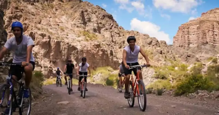 Grupo de ciclistas en ruta entre acantilados rocosos en paisaje árido con vegetación escasa