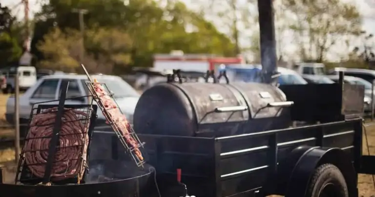 Parrilla ahumadora sobre un remolque negro, con chorizos asándose al lado