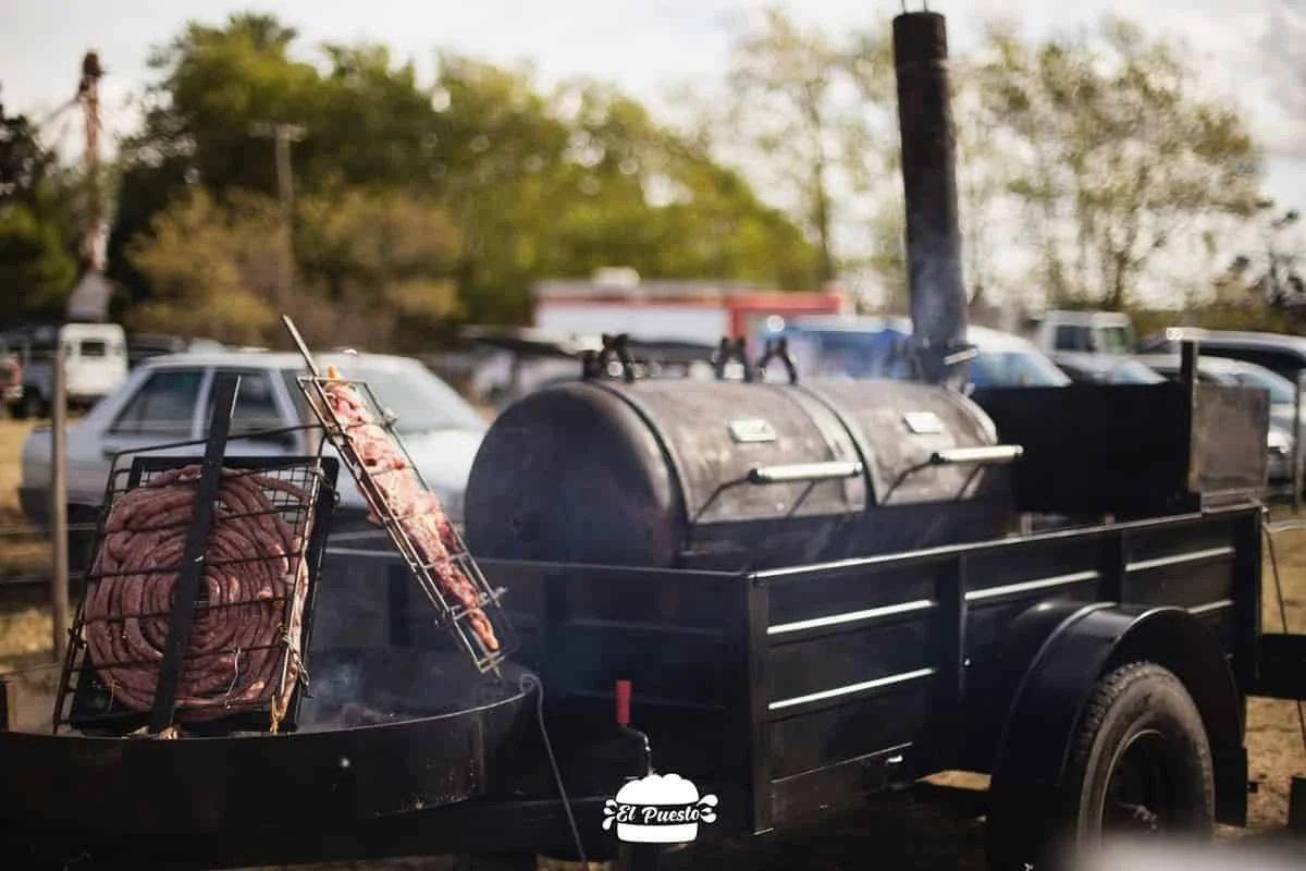 Parrilla ahumadora sobre un remolque negro, con chorizos asándose al lado