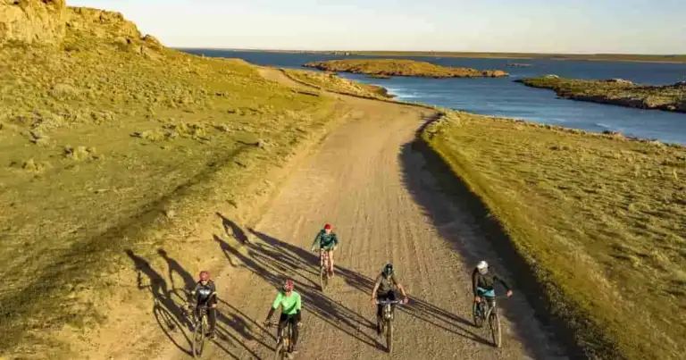 Ciclistas en ruta de tierra en meseta con vistas a costa azul y llanura verde extendida