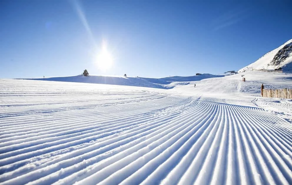 Pista de esquí preparada con líneas de surcos y montañas nevadas