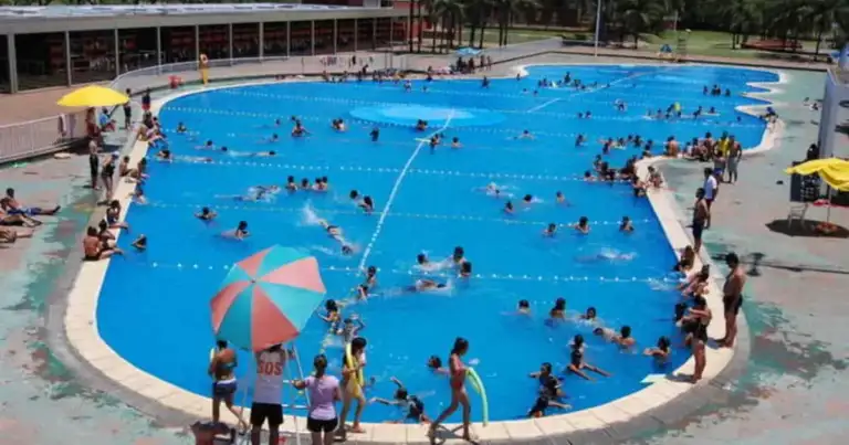 Piscina olímpica de color azul intenso llena de bañistas bajo cielo nublado