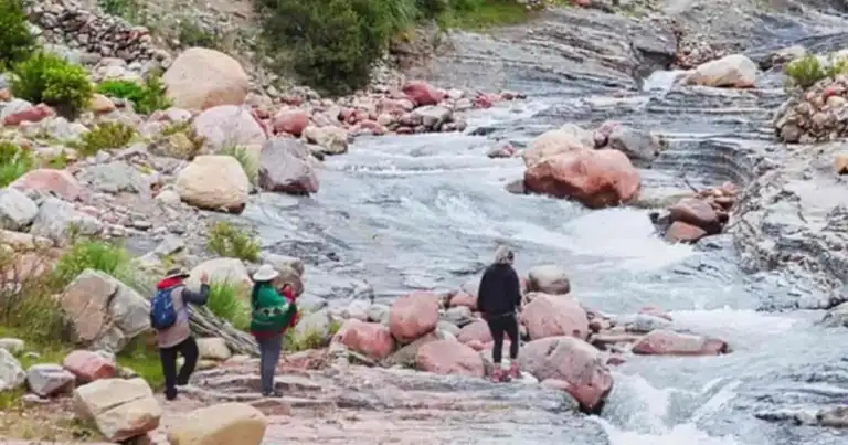 Turistas explorando rocas junto a río alpino rápido en cañón rodeado de vegetación