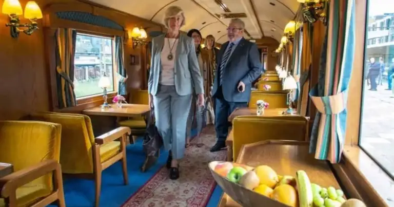 Interior de tren de lujo con pasajeros caminando entre asientos dorados y lámparas clásicas
