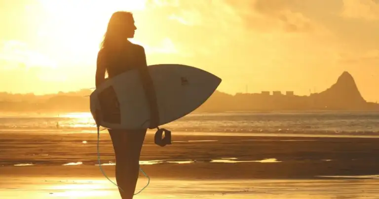 Surfista con tabla al atardecer en playa con silueta contra sol