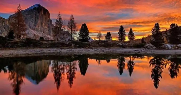 Atardecer rojo intenso sobre montaña rocosa reflejado en lago sereno