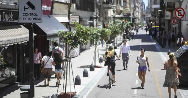 Calle peatonal con árboles, personas caminando y señales de tránsito