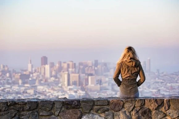 Mujer de cabello largo mirando desde una altura hacia una ciudad lejana