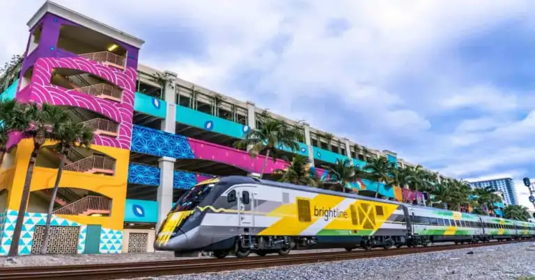 Tren Brightline amarillo y azul en estación bajo estructura colorida