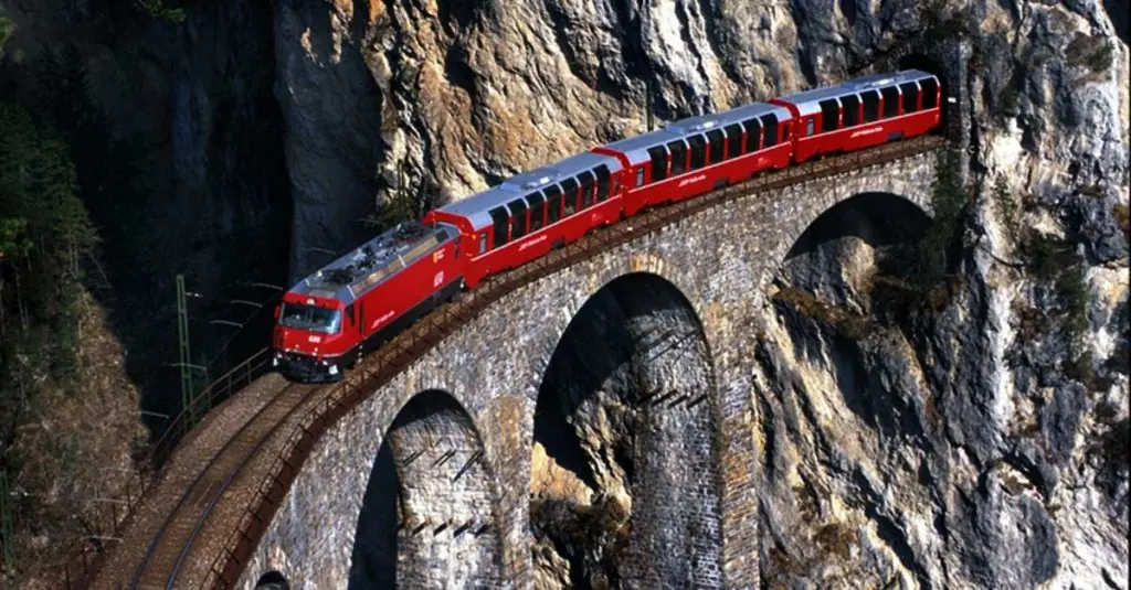 Tren rojo en viaducto de piedra sobre montaña rocosa