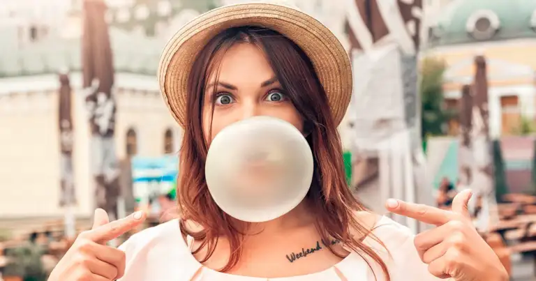 Mujer con sombrero de paja vistiendo camiseta blanca soplando chicle