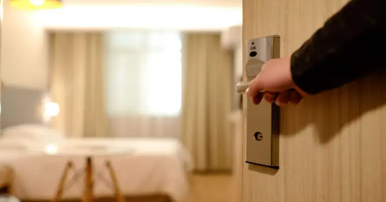 Mano abriendo puerta de habitación de hotel con cama visible