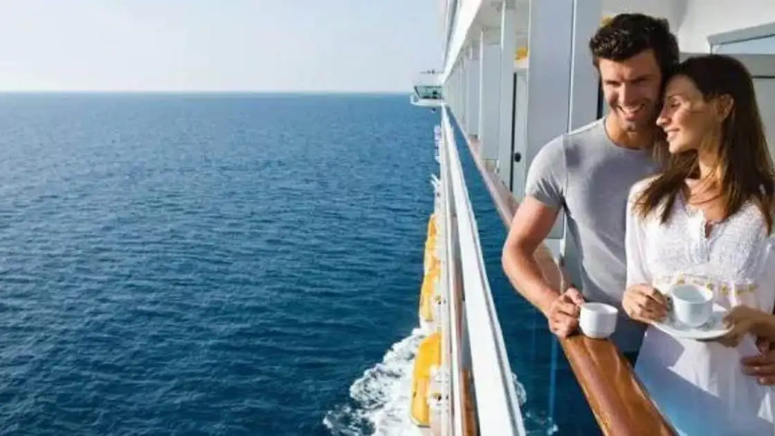 Pareja sonriendo apoyada en baranda de crucero con océano y cielo despejado