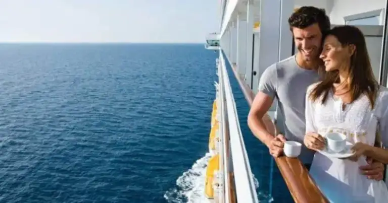Pareja sonriendo apoyada en baranda de crucero con océano y cielo despejado