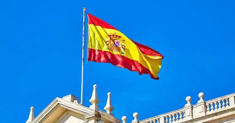 Bandera española ondeando sobre edificio blanco con columnas clásicas