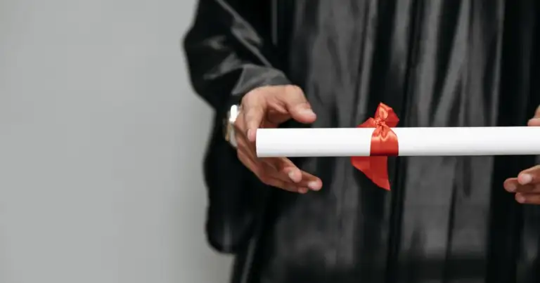 Manos sosteniendo diploma atado con cinta roja
