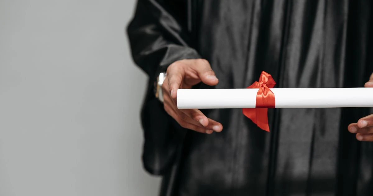 Manos sosteniendo diploma atado con cinta roja