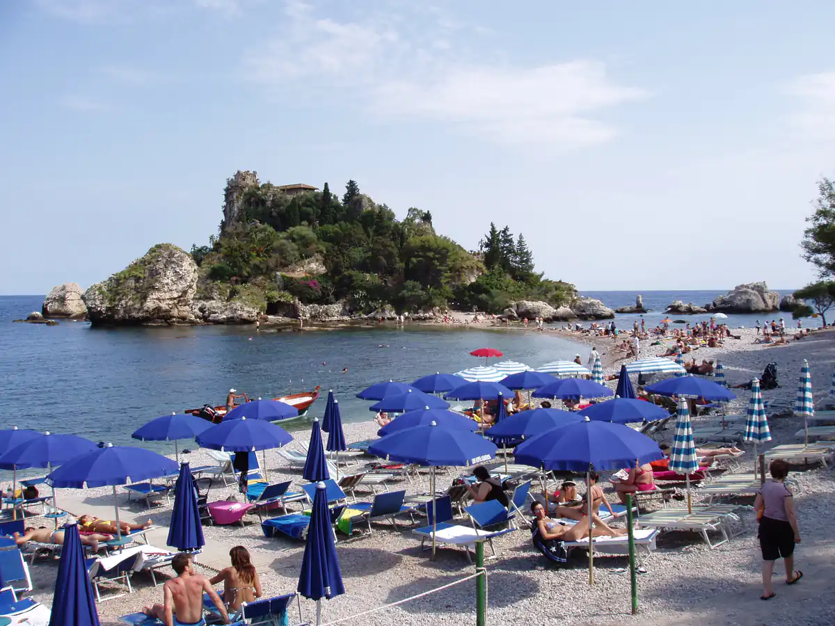 Isola Bella en Taormina con playa rodeada de parasoles azules y piscina natural