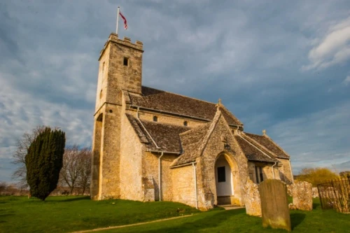 Iglesia medieval de piedra de Swinbrook con su torre y el cementerio entre prados verdes