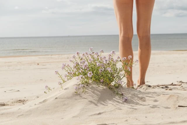 Piernas de una persona caminando sobre arena en una playa natural, típica de destinos nudistas tranquilos
