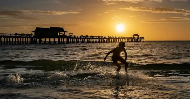 Surfista en el mar durante el atardecer en el muelle de Naples, Florida.