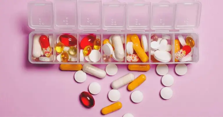 Organizador de medicamentos en compartimentos sobre fondo rosa con píldoras dispersas