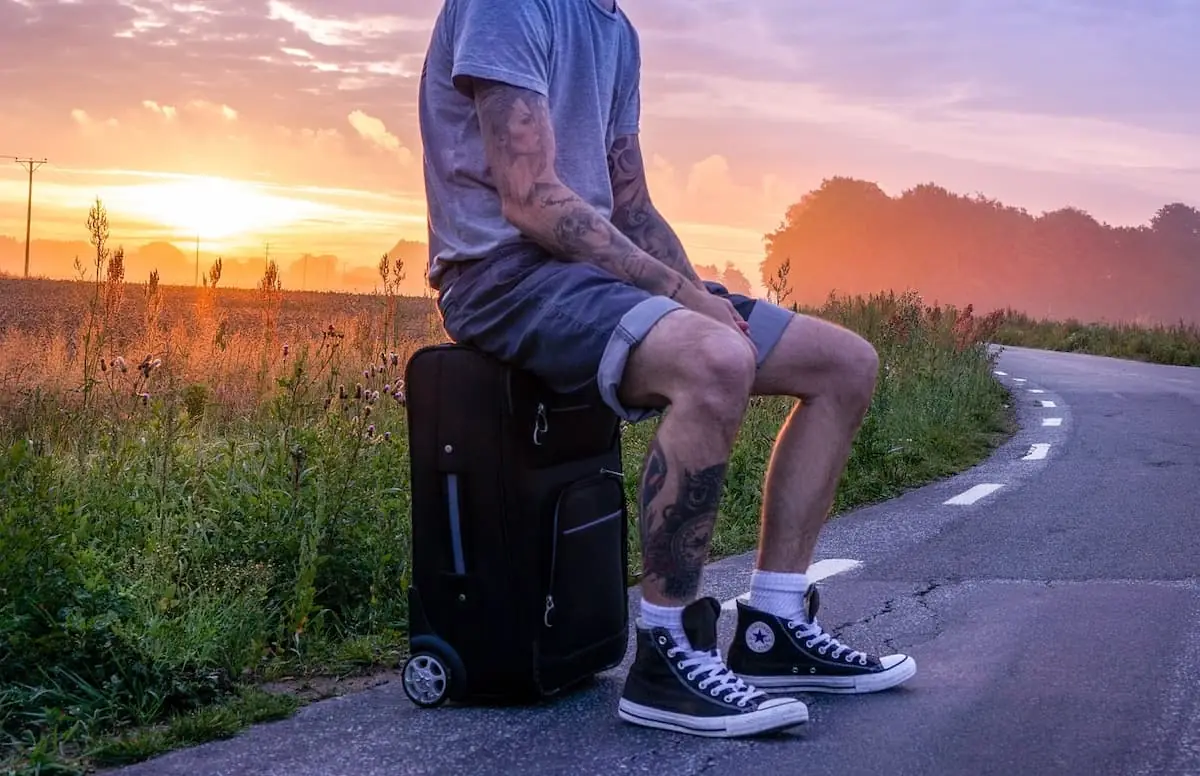 Viajero descansa sentado en su maleta junto a la carretera al atardecer