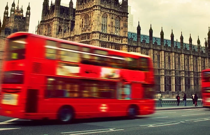 Autobús rojo de dos pisos en movimiento frente a Palacio de Westminster en Londres