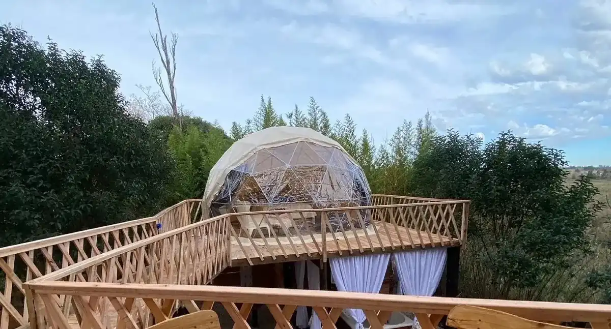 Domo geodésico de glamping elevado sobre plataforma de madera en bosque
