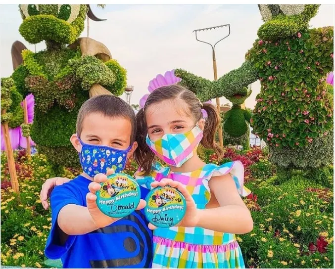 Dos niños con pins de Disney en jardín de figuras topiary recortadas
