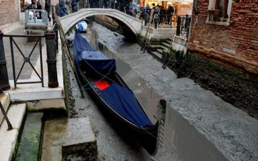 Góndola azul bajo puente arqueado en canal poco profundo de Venecia