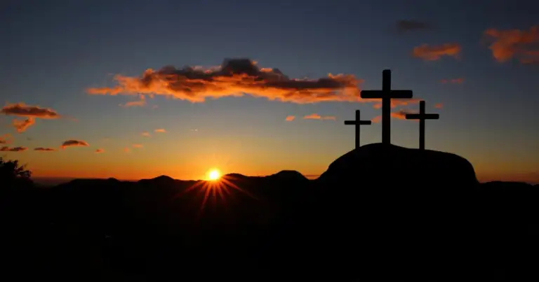 Tres cruces en silueta al atardecer con cielo naranja