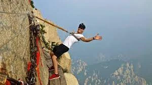 Alpinista en vía ferrata en pared rocosa vertical con montaña al fondo