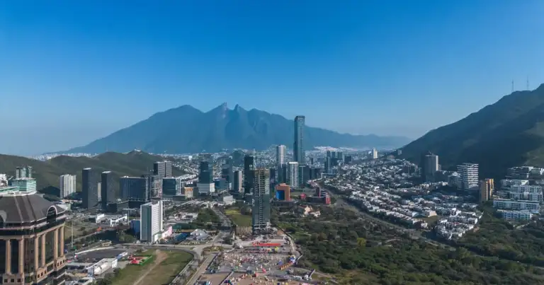 Vista panorámica de Monterrey rodeada de montañas, con edificios modernos, zonas residenciales y paisajes naturales que muestran el contraste urbano y serrano de la ciudad.