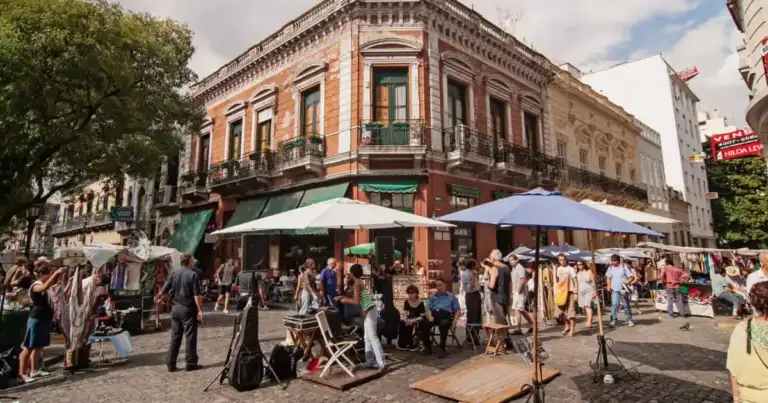 Edificio colonial con fachada roja, personas bajo sombrillas en la terraza