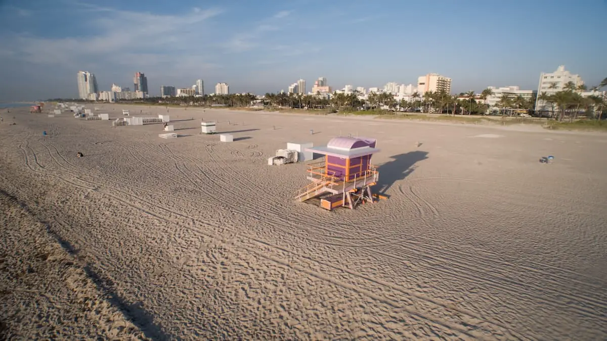 Playa arenosa con casetas de vigilancia de colores y horizonte urbano