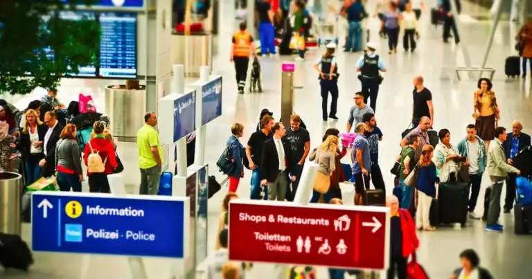 Interior de terminal de aeropuerto con señales de información y muchas personas