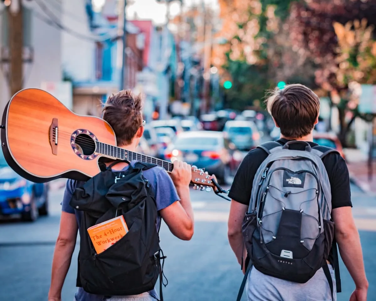 Dos viajeros jóvenes con mochilas, uno con guitarra