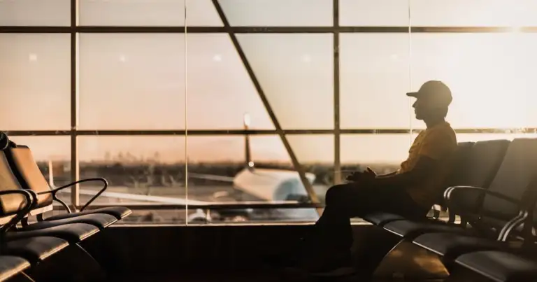 Pasajero en terminal de aeropuerto viendo el atardecer a través de ventanas