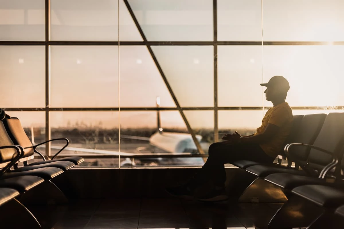 Pasajero en terminal de aeropuerto viendo el atardecer a través de ventanas