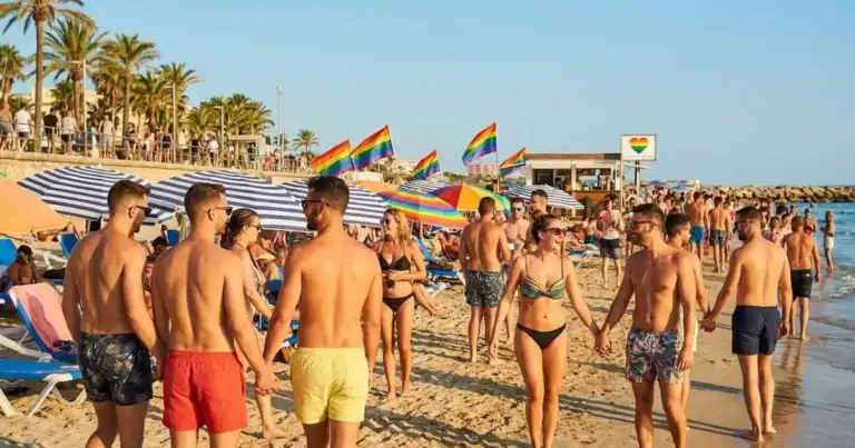 Playa LGBT con banderas arcoíris y parejas disfrutando de un destino de turismo rosa.