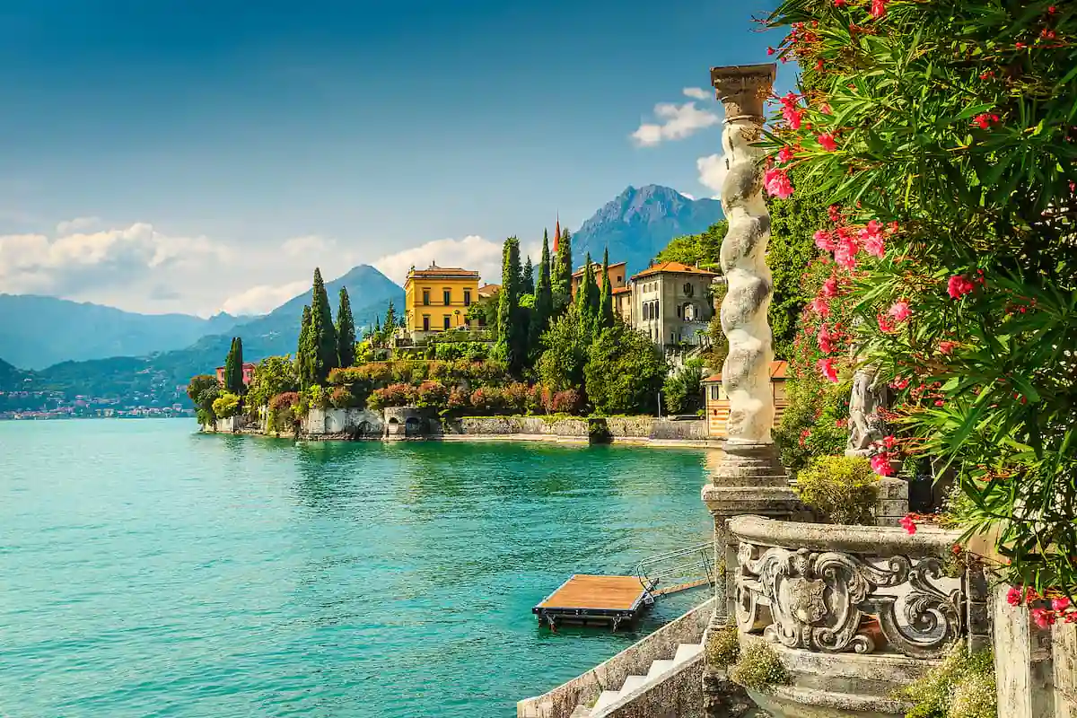 Villa italiana junto a lago turquesa con montañas y cipreses