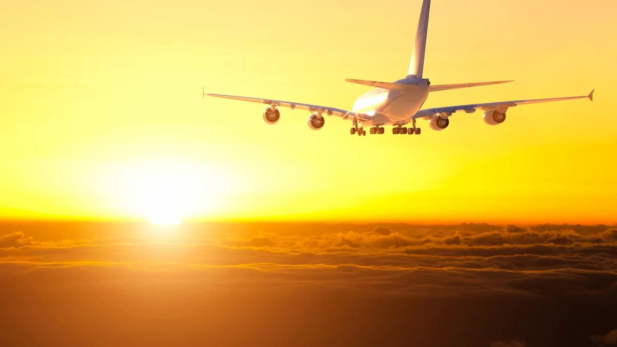 Avión en silueta volando hacia el sol en atardecer dorado