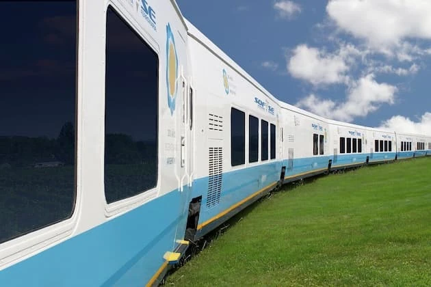Tren turístico blanco y turquesa en paisaje de montañas verdes