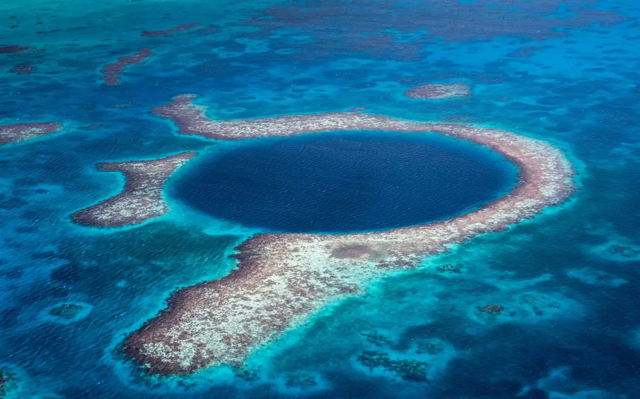 Cenote azul oscuro rodeado de agua turquesa y arrecife