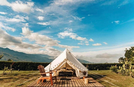 Carpa glamping blanca con silla Adirondack en plataforma de madera, montañas al fondo