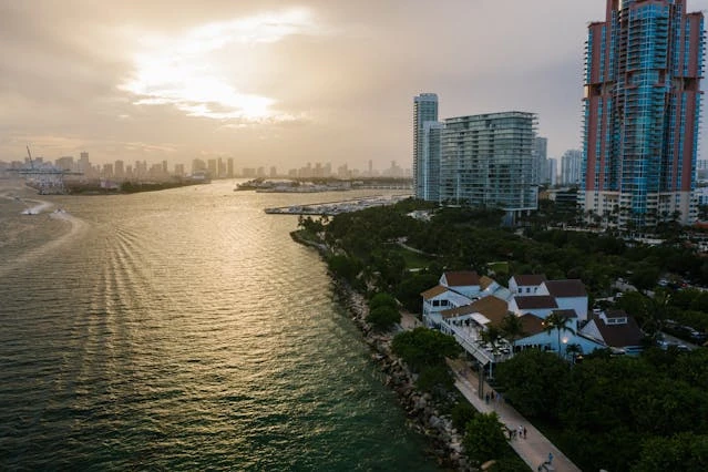 Vista aérea de Miami al atardecer con edificios frente al mar y barcos en la bahía.