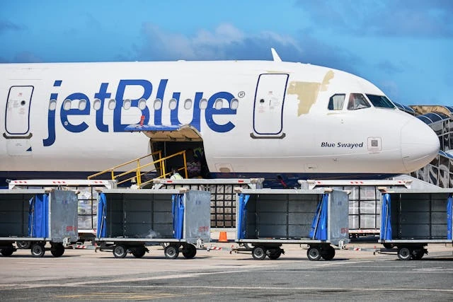 Avión de JetBlue en tierra con compartimento de equipaje abierto y carros de carga.